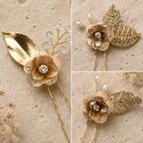 Three views of a gold and beige floral hair pin accessory set on a textured beige stone background. The set includes a beige flower with a clear crystal center and gold leaf accents, pearl details, and a gold rhinestone-embellished leaf piece.