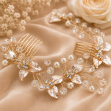 Two gold bridal hair combs decorated with faux pearls, clear crystal beads, and gold-toned floral leaf motifs, arranged on a beige satin fabric with dried flowers and a rose in the background.