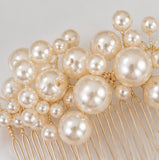 A gold-tone hair comb decorated with multiple cream and ivory faux pearls of varying sizes, shown against a light neutral background.