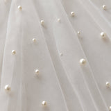 Close-up of a white tulle fabric with scattered small pearl beads and a few tiny rhinestone accents, showing the sheer mesh texture and soft folds.