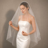 A bride wearing a strapless white wedding dress and a sheer white tulle veil adorned with small scattered rhinestones, posed against a neutral gray studio background.
