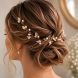 A woman shown from the back wearing a bridal hair accessory with gold-toned leaf-shaped charms and small white pearl-like beads woven into an updo.