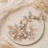 A delicate floral hair accessory with rose gold wire, silver leaf embellishments, and white pearl beads, displayed on a round beige stone plate with dried baby's breath flowers.